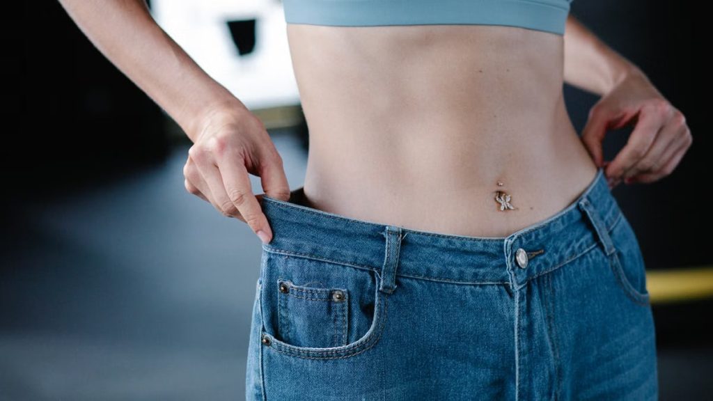 Close-up of woman pulling oversized jeans, illustrating weight loss.